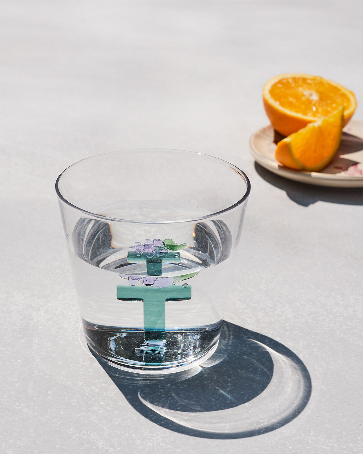 Clear Alphabet glass with a teal letter T and purple flowers, half filled with water.