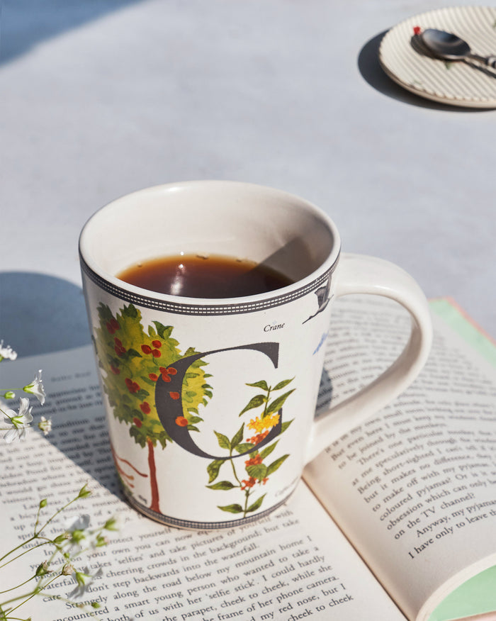 Chameli mug with letter C and botanical print, filled with coffee on a book.