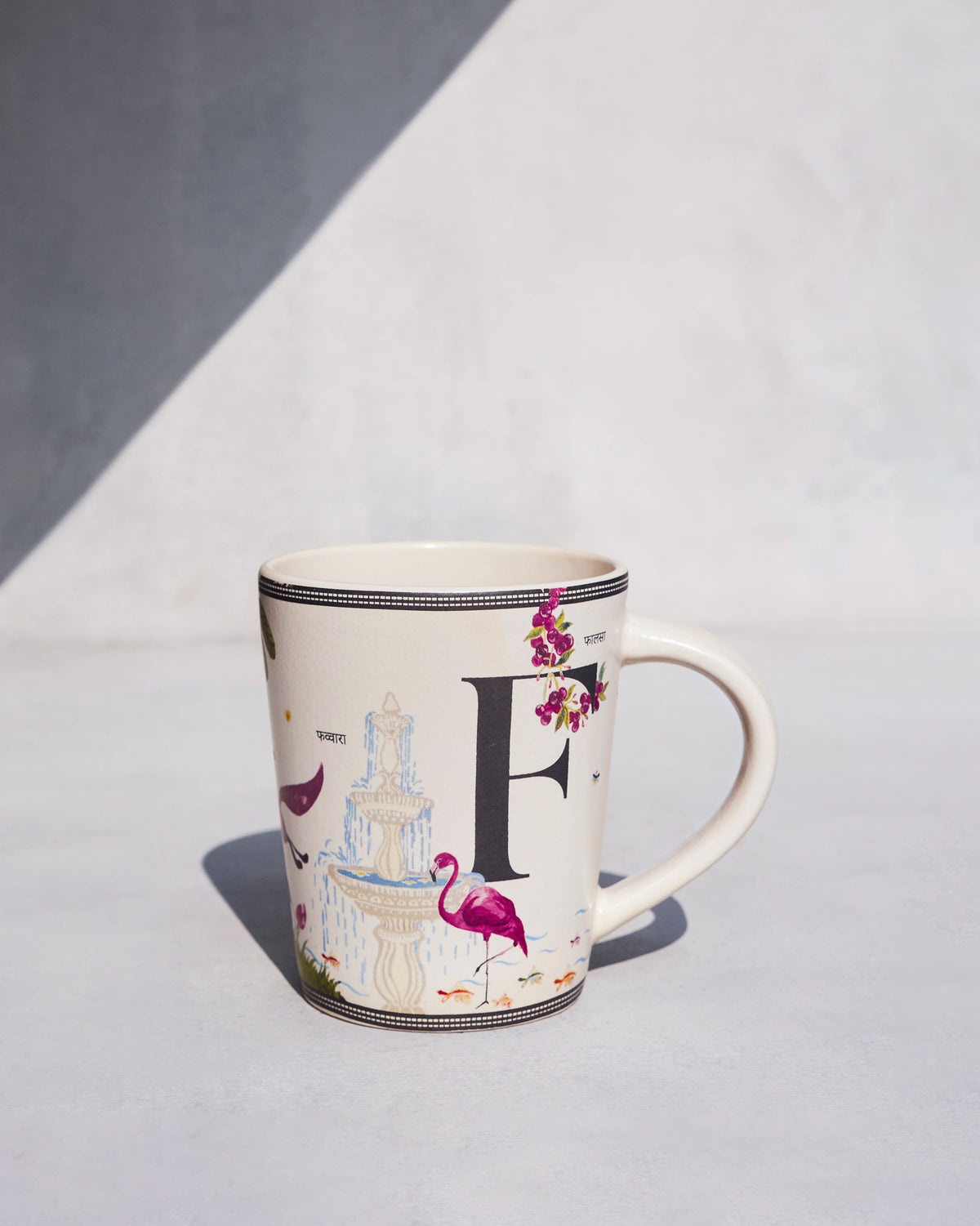 Cream Firefly mug with a black letter F, pink flamingo, and fountain motif.