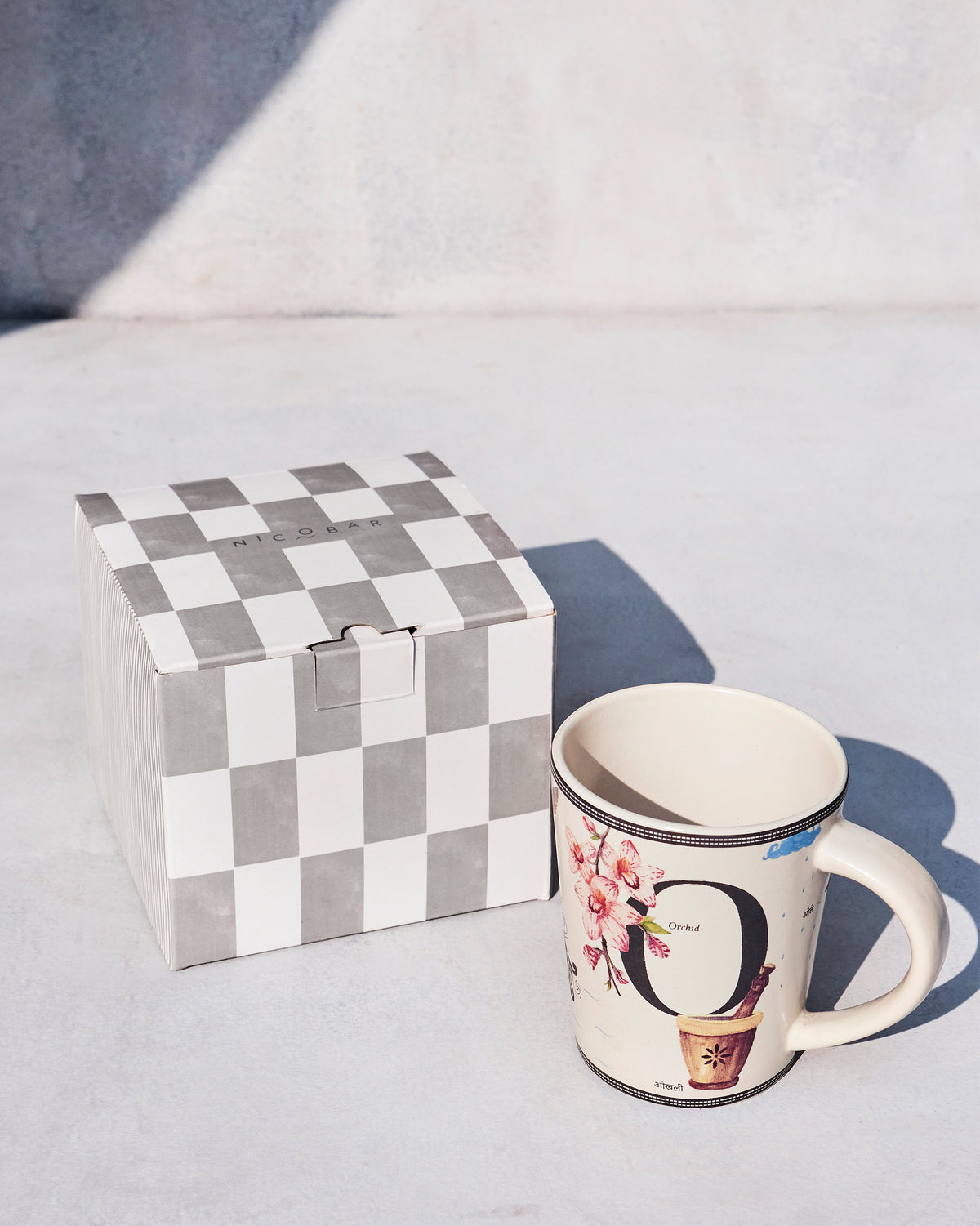 Cream Owl mug with orchid print beside a grey checkerboard Nicobar box.