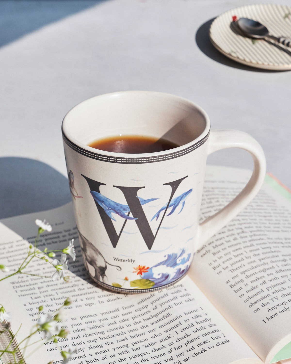 Waterlily mug with a large W and whale print resting on an open book.