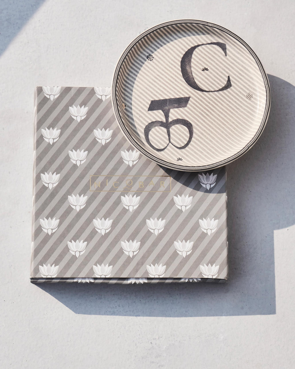 Akshar Coaster - C resting on its grey lotus-print box.