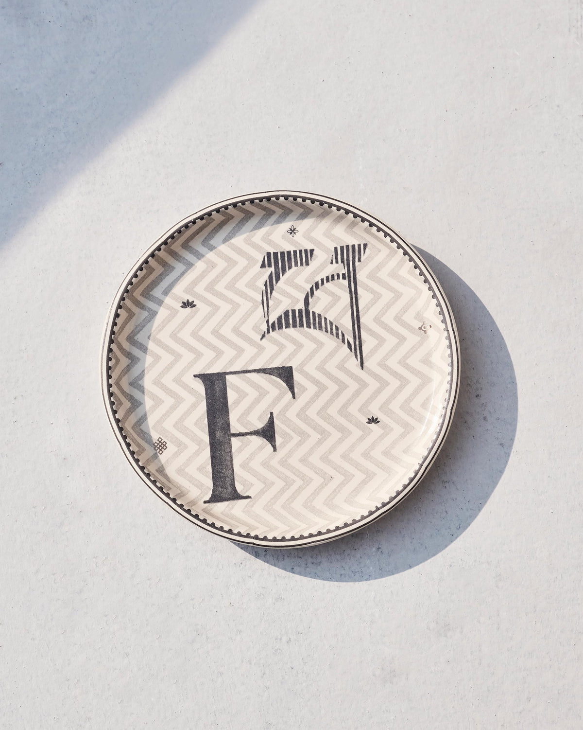 Akshar Coaster - F lying flat, showing its beaded rim and grey F glyph.
