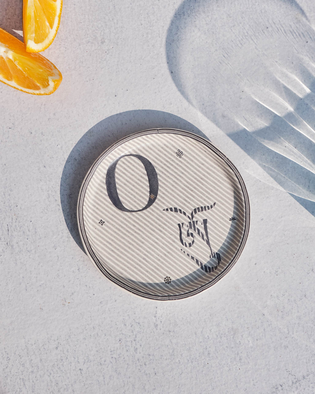 Akshar Coaster - O laid flat, showing the grey O glyph on diagonal stripes.