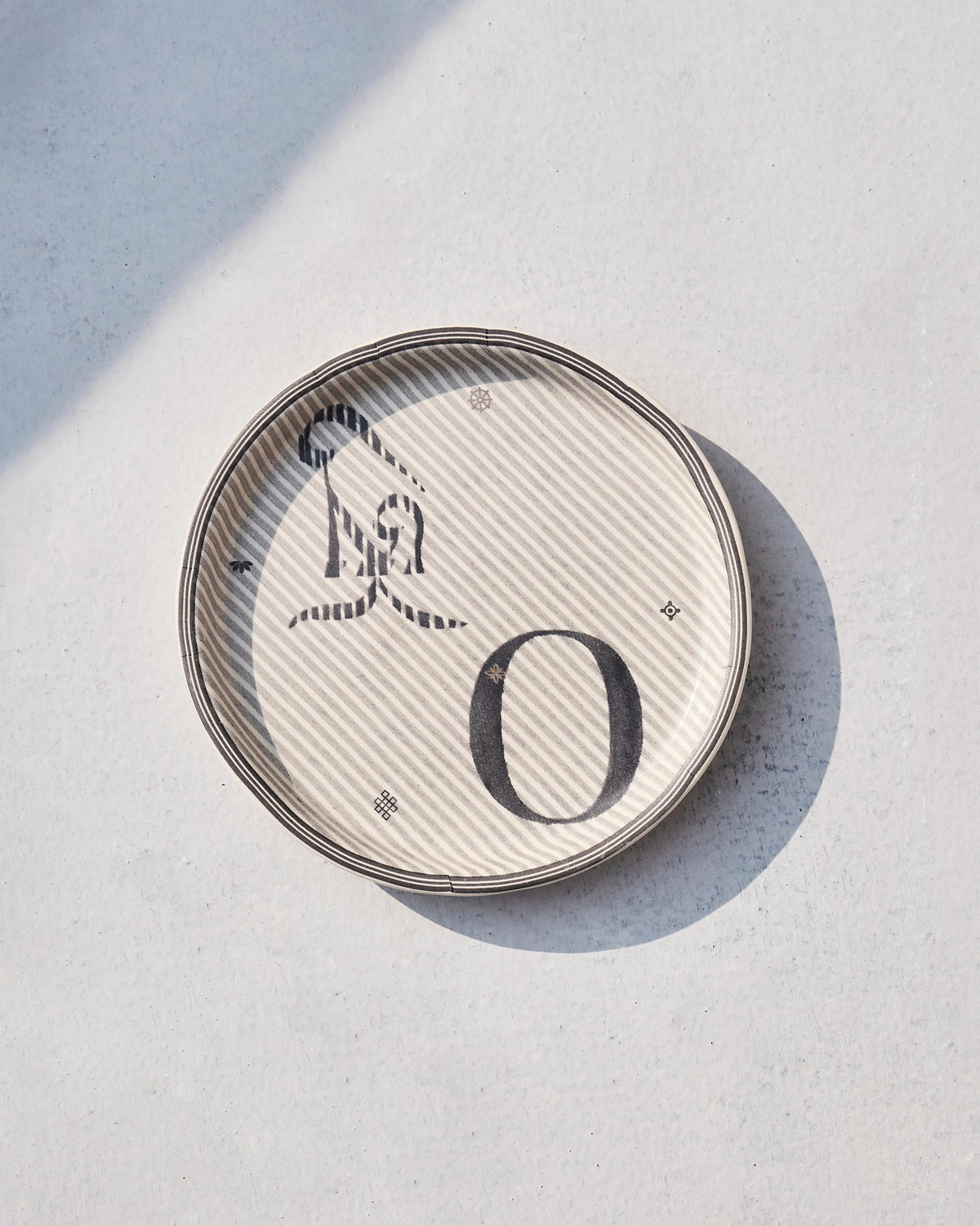 Akshar Coaster - O lying flat, showing its beaded rim and grey O glyph.