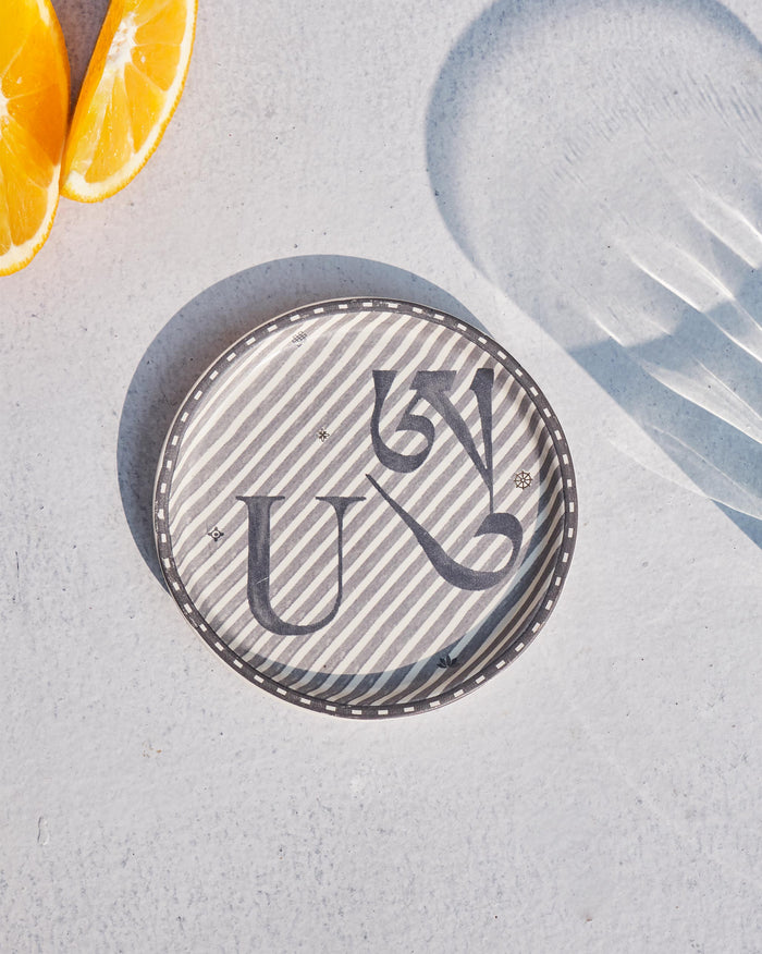 Akshar Coaster - U laid flat, showing the grey U glyph on diagonal stripes.