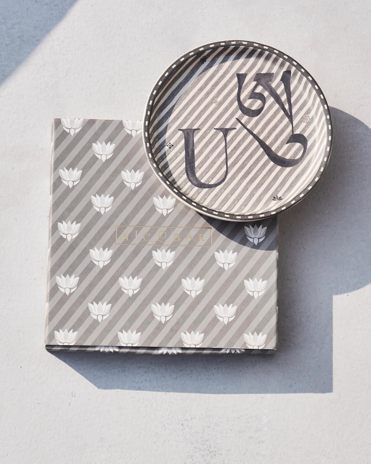 Akshar Coaster - U resting on its grey lotus-print box.