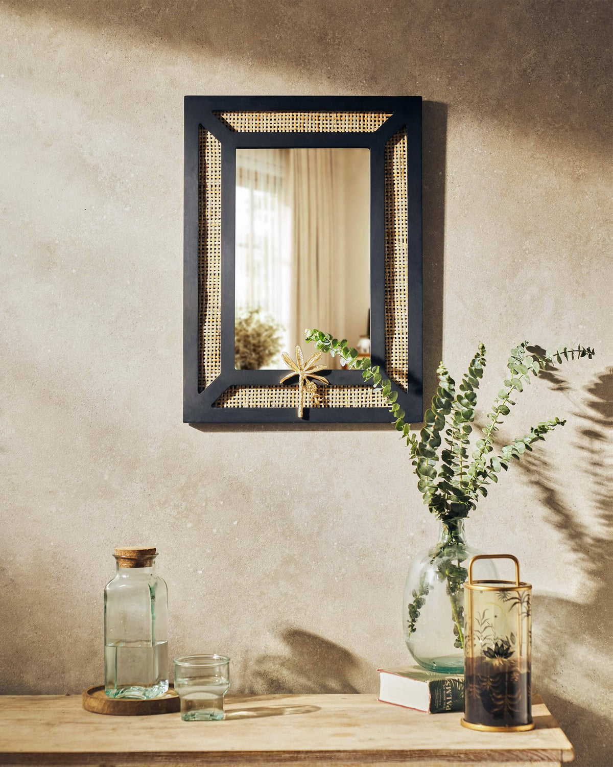 Pondicherry Mirror with a black cane-panelled frame and a gold ornament at its base.