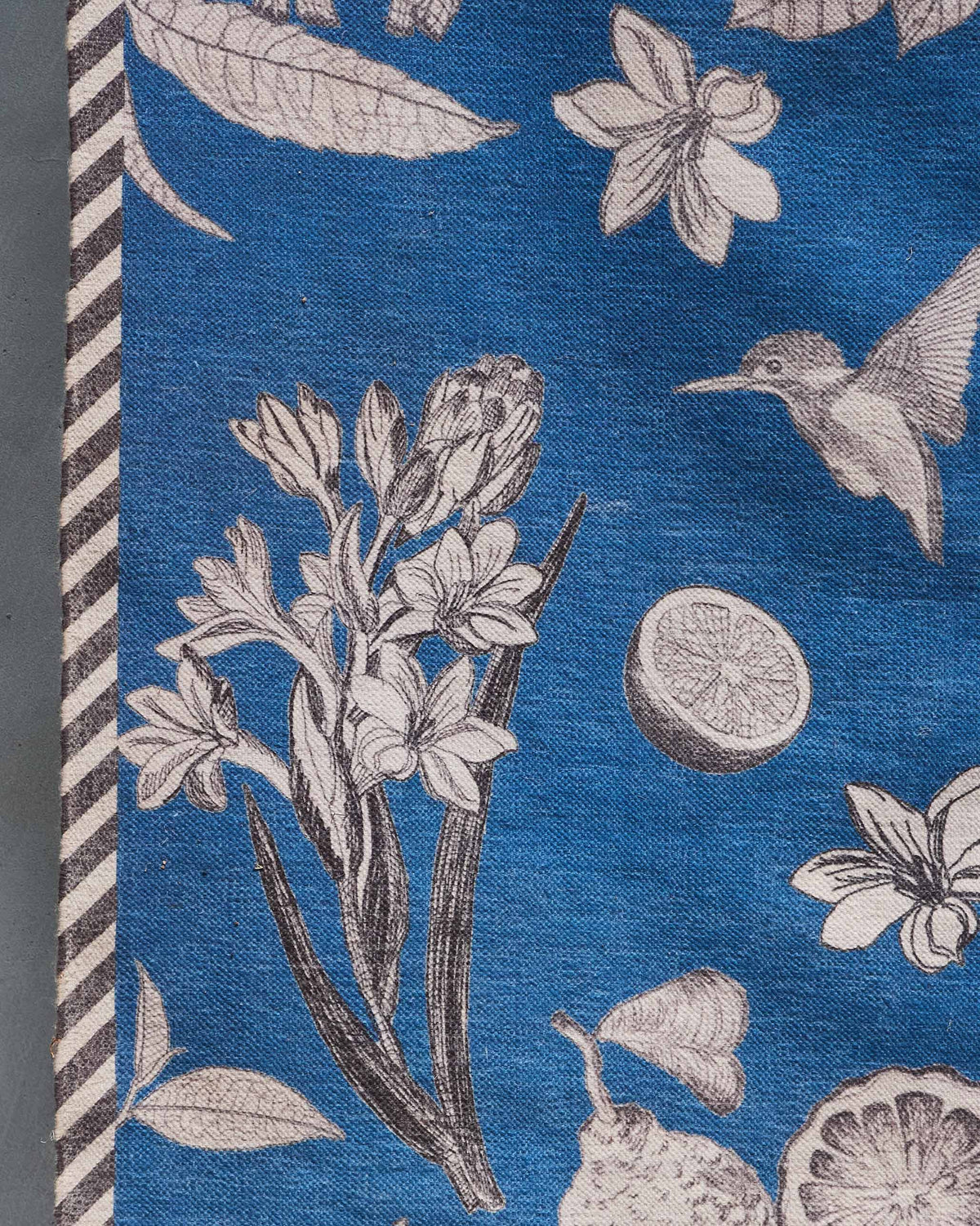 Close-up of Forest Rug in navy corner with a hummingbird, flowers and lemon slice.