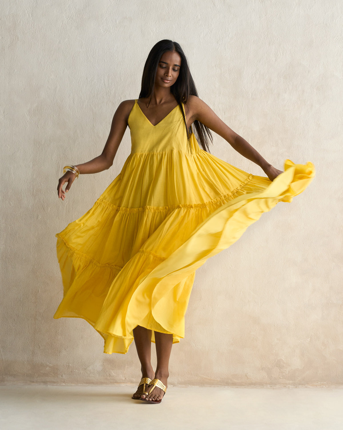 Person holding out a yellow tiered maxi dress to show the flared skirt.