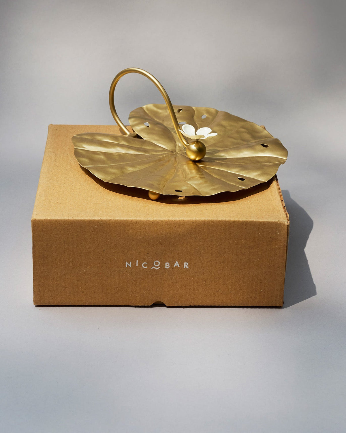 Gold Padma napkin holder resting on its brown Nicobar gift box.