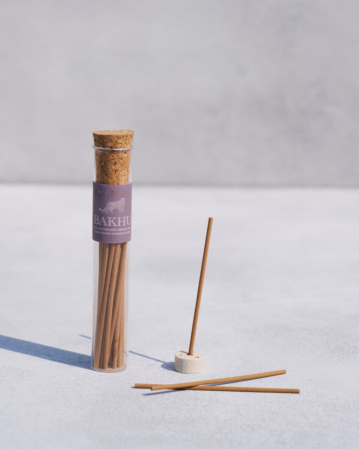 Bakhu incense sticks in a tube with one stick standing in a white holder.