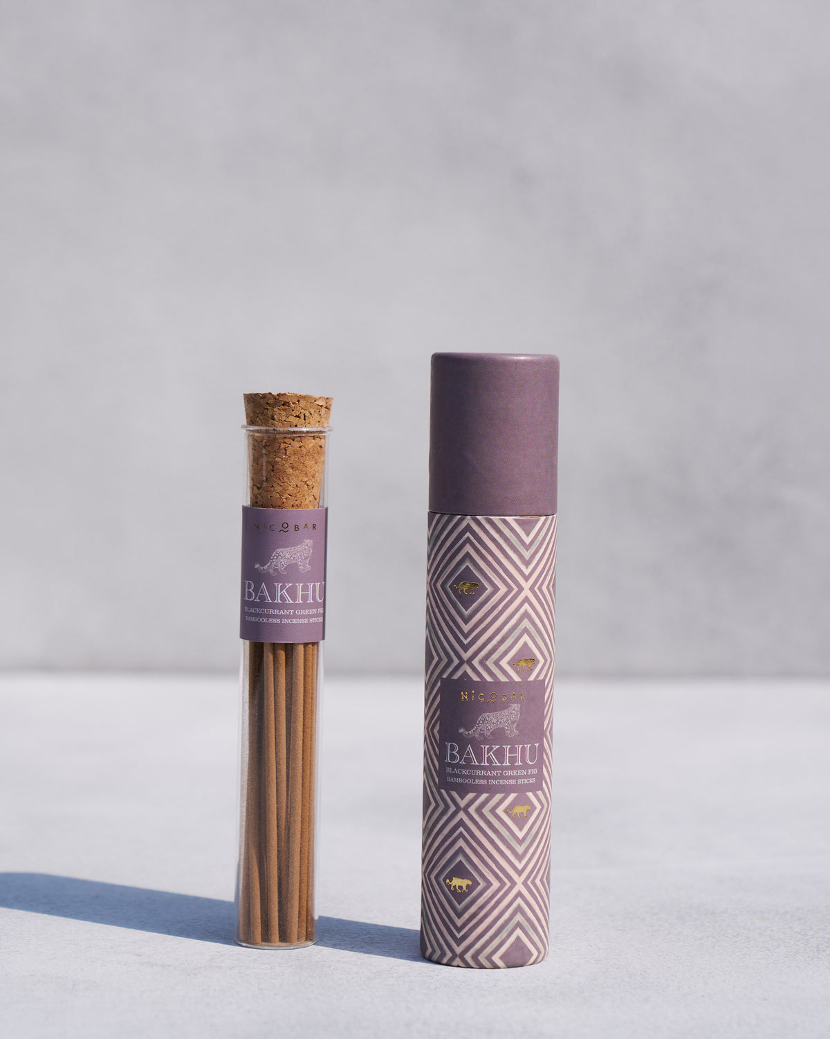 Bakhu incense sticks in a tube beside their patterned purple box.
