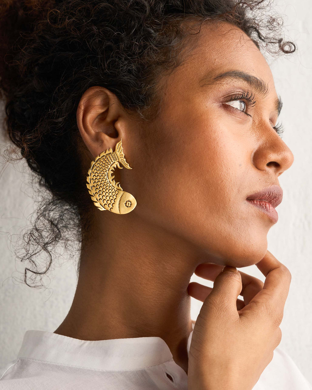 Side profile of gold Meen Earrings worn on a person.
