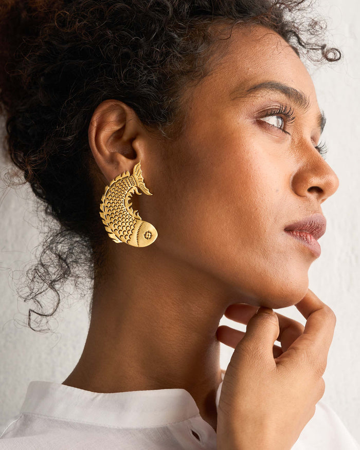 Side profile of gold Meen Earrings worn on a person.