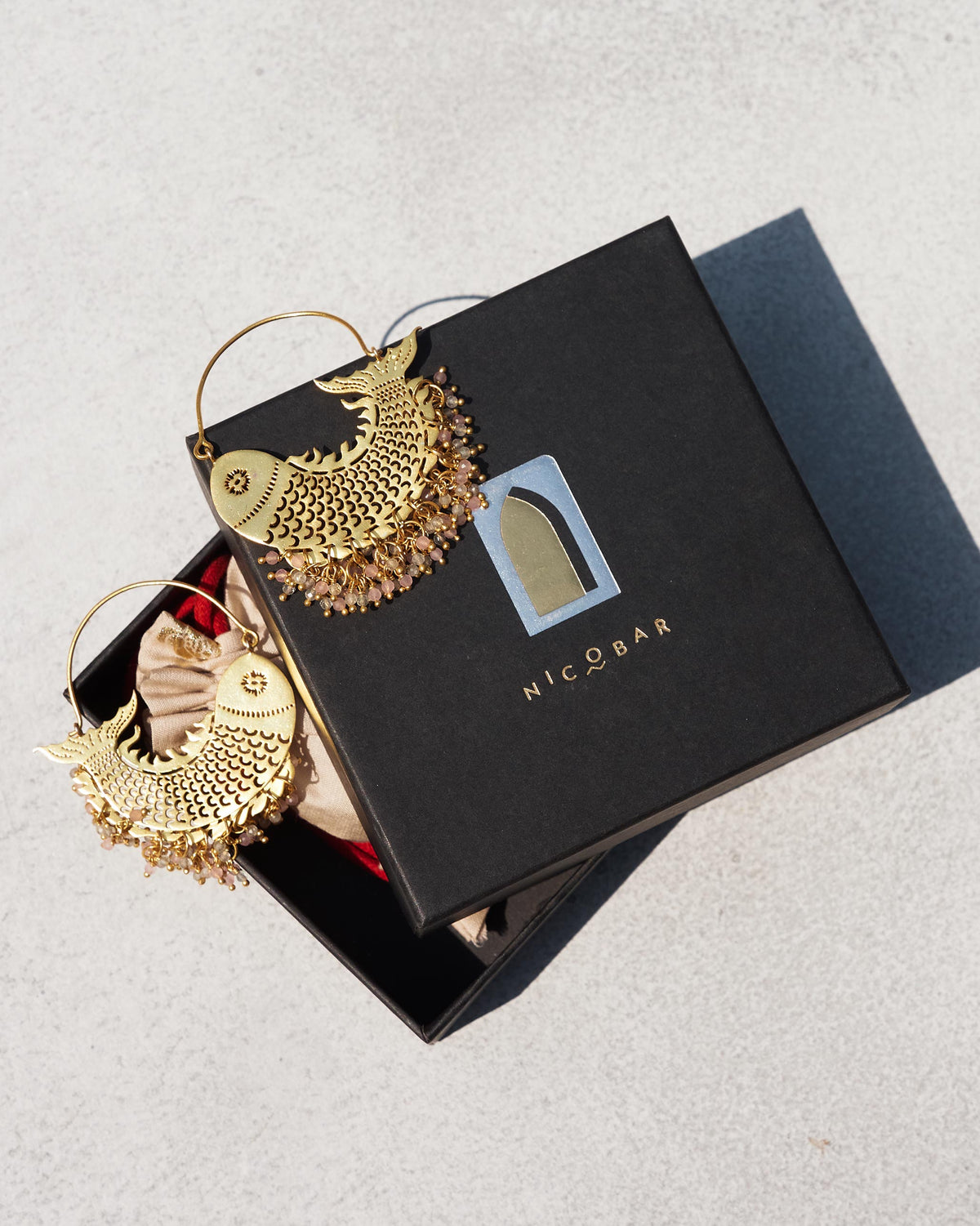 Pair of gold Meen Bali with fish motifs beside a black gift box.