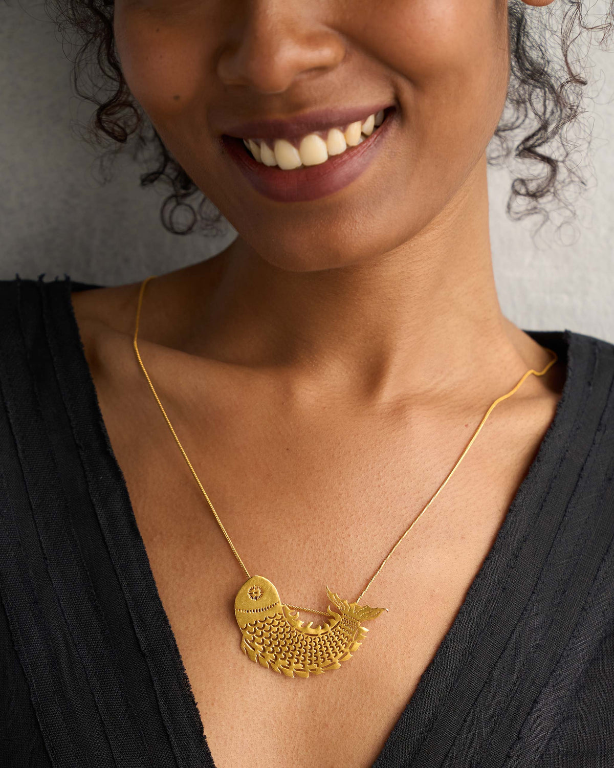 Close-up of a gold Meen Pendant worn on a black top.