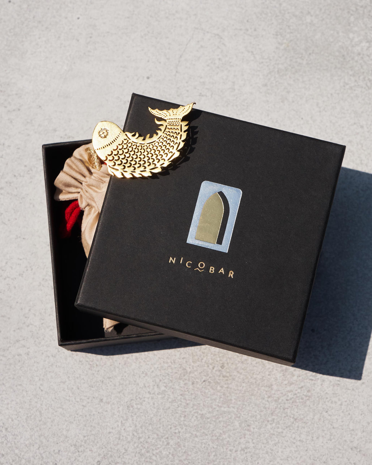 Gold Meen Pendant resting on a Nicobar gift box.