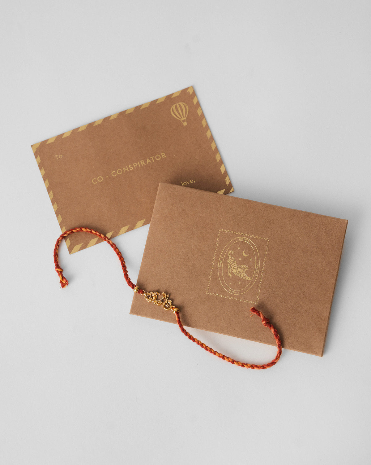 Motor Cycle Rakhi with a red braided thread beside a kraft gift card.
