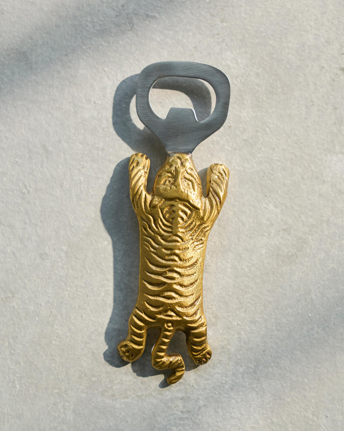 Gold Sumatran tiger bottle opener with a silver head laid flat.