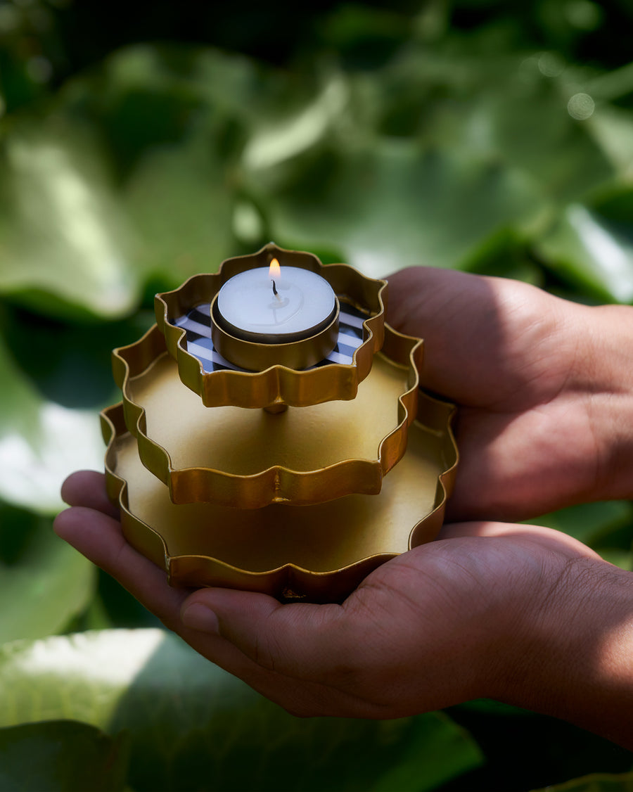 Hands holding the lit gold Sama votive among green leaves