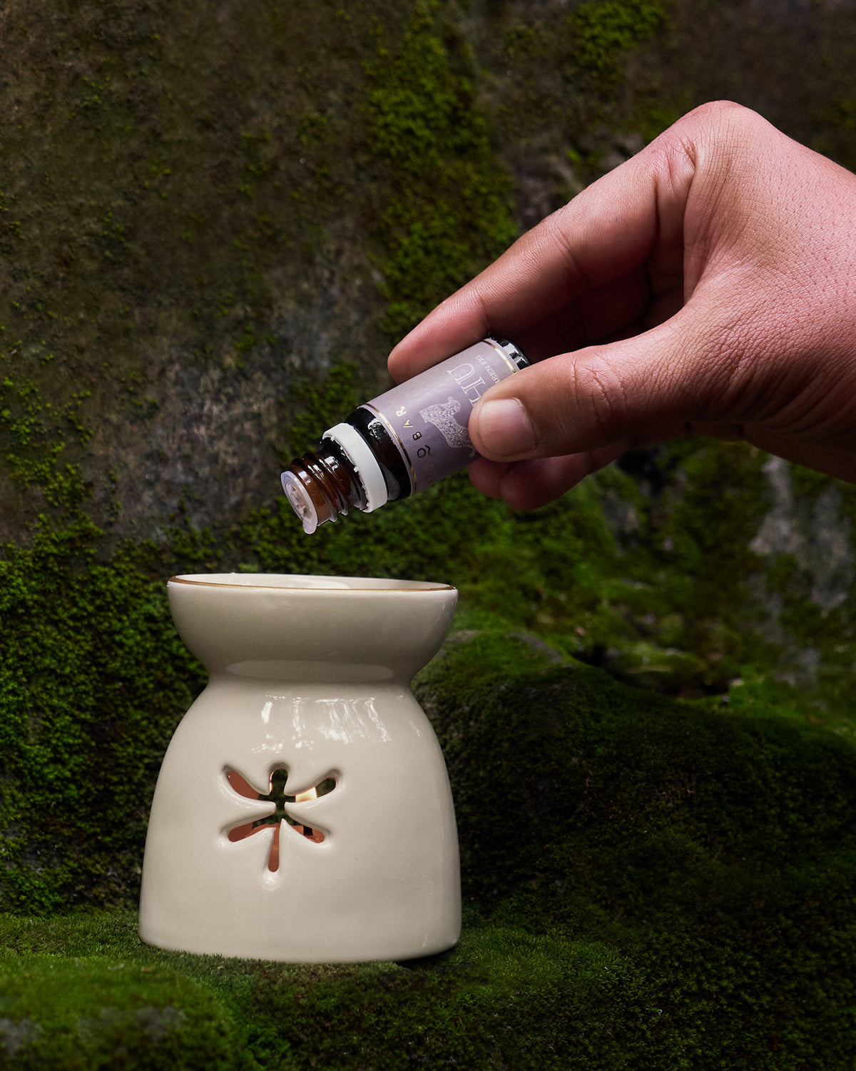 Person adding oil to a cream ceramic oil burner from a small bottle.