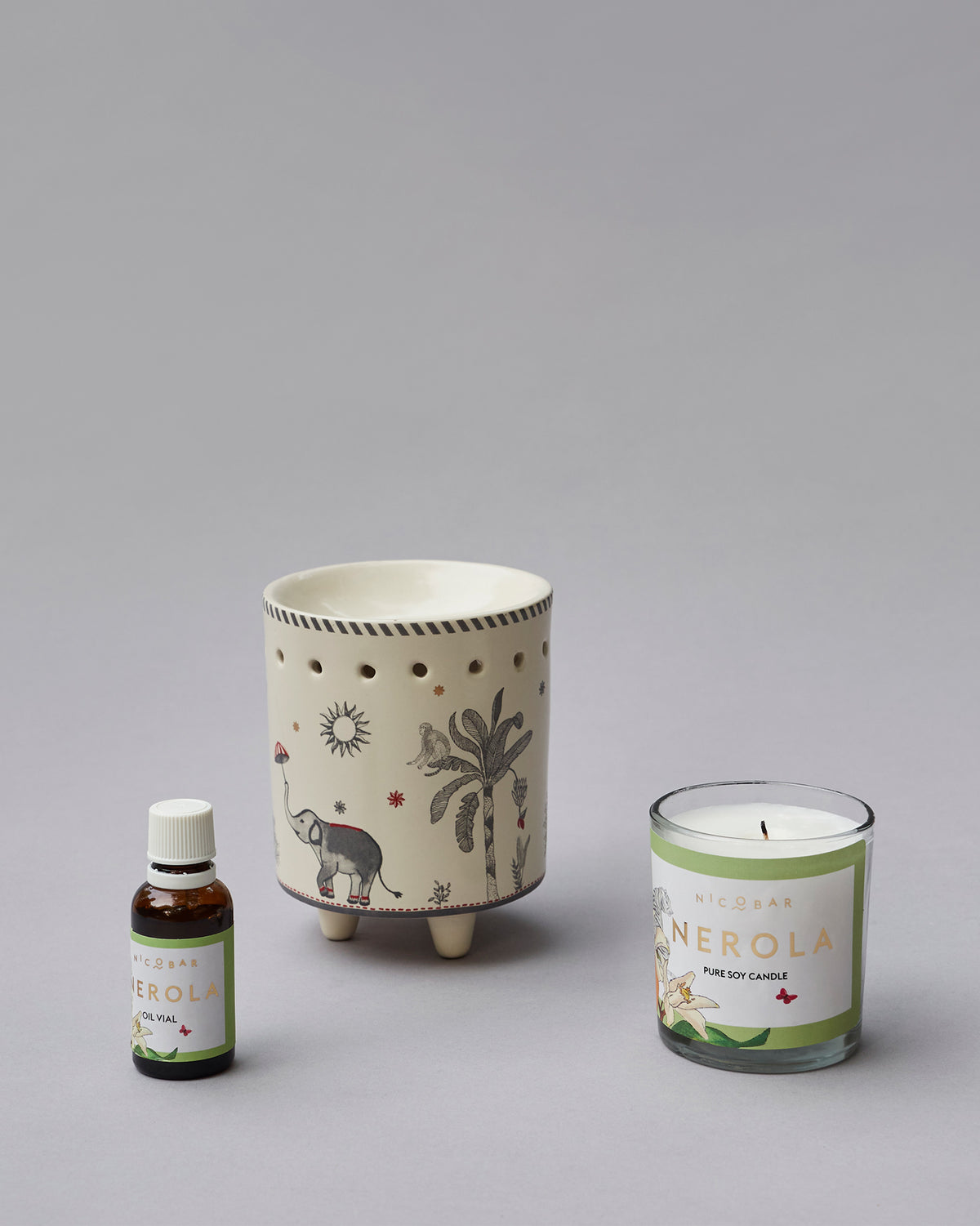 Ceramic burner with an elephant and palm design, beside an oil vial and soy candle.
