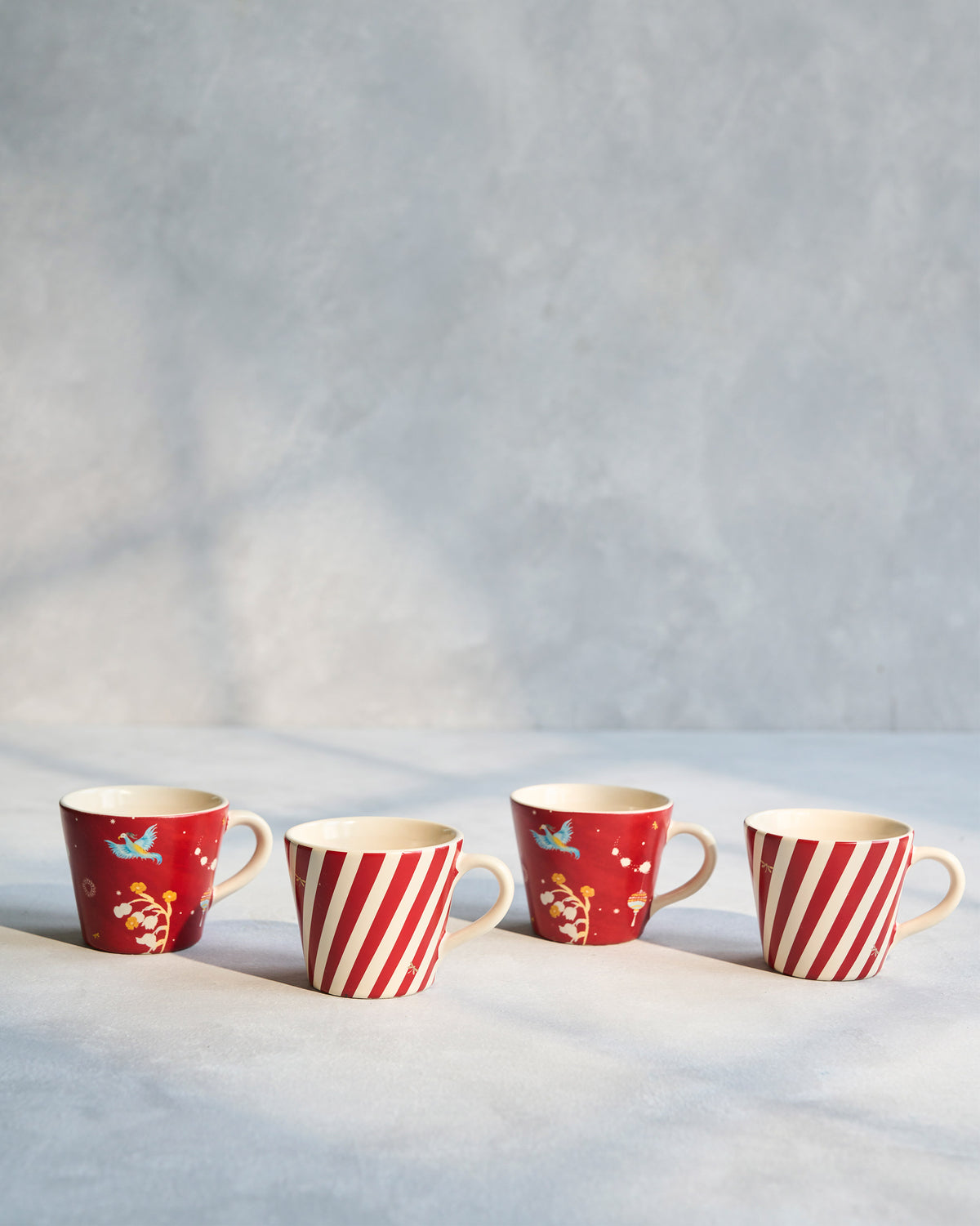 Row of four Phoenix espresso mugs in stripe and bird-print designs.