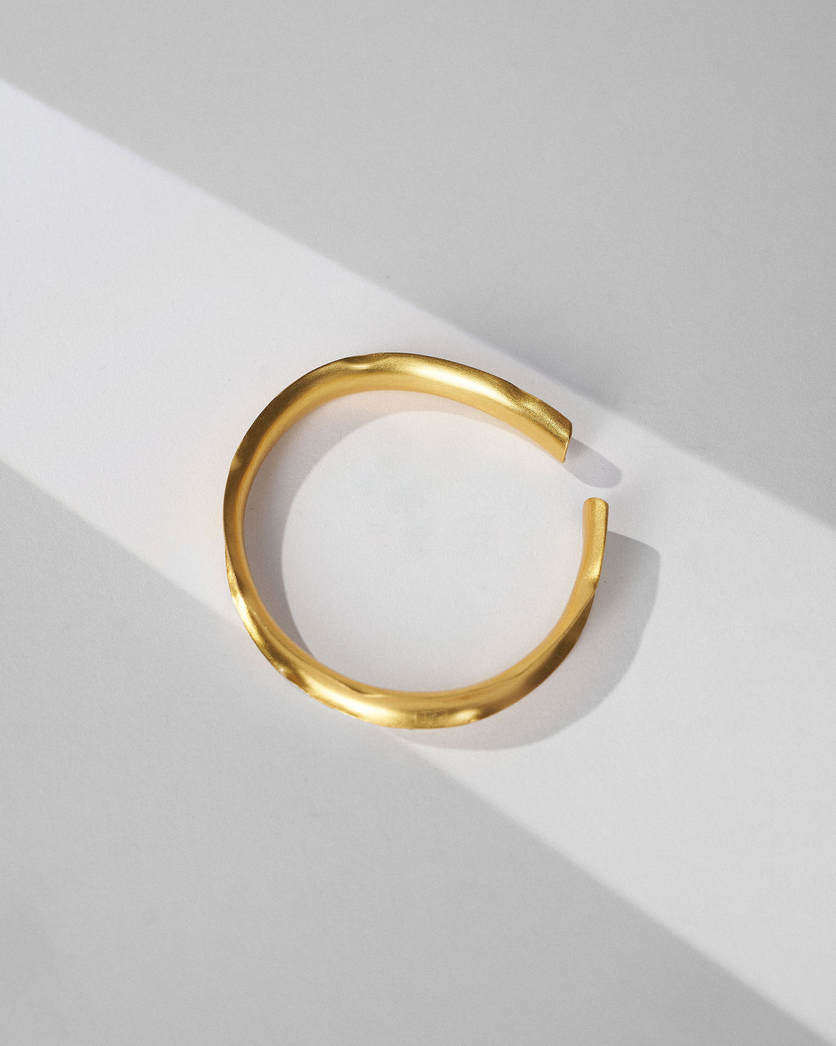 Gold Batur thin cuff bangle showing its open ends and wavy surface.