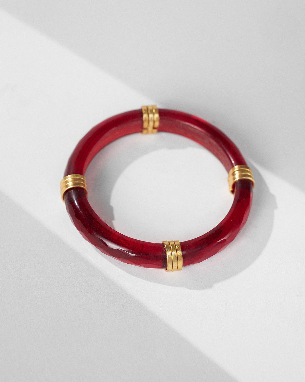 Translucent red glass bangle with four gold-toned ribbed accents on white.