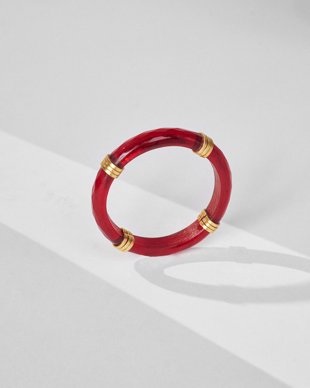 Upright translucent red glass bangle showing its thickness and gold accents.