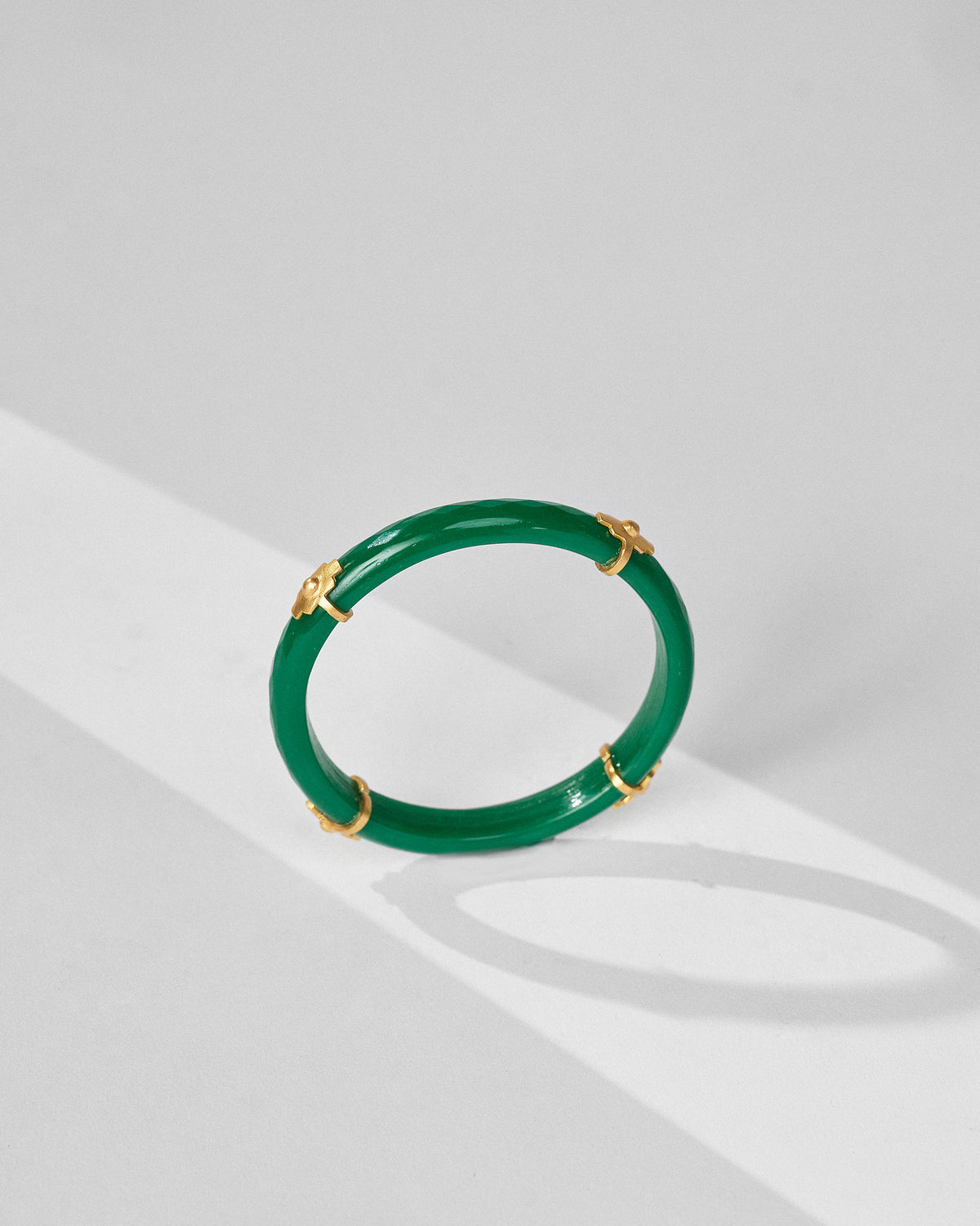 Upright glossy green glass bangle with gold floral spacers on white.