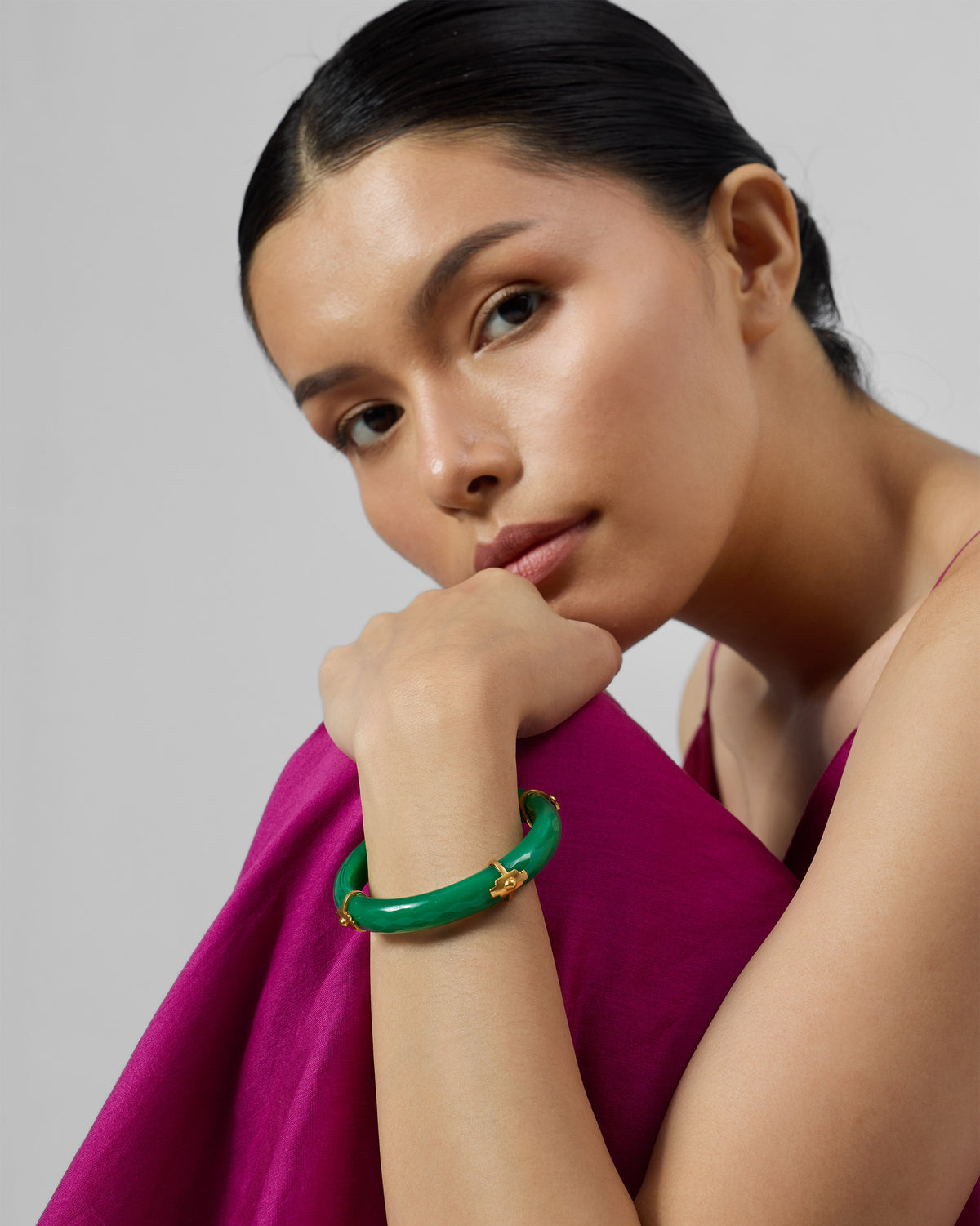 Glossy green glass bangle with gold accents worn on a wrist.