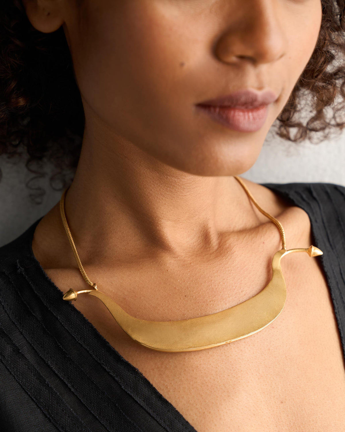 Close-up of a gold Musafir Necklace worn on a person, showing the curved bar.