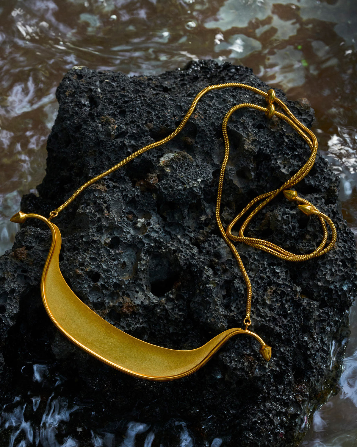 Gold Musafir Necklace laid out in a loop, showing the curved bar and chain.
