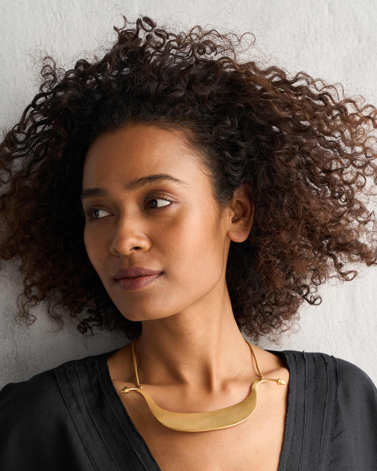 Person wearing a gold Musafir Necklace with a curved bar.