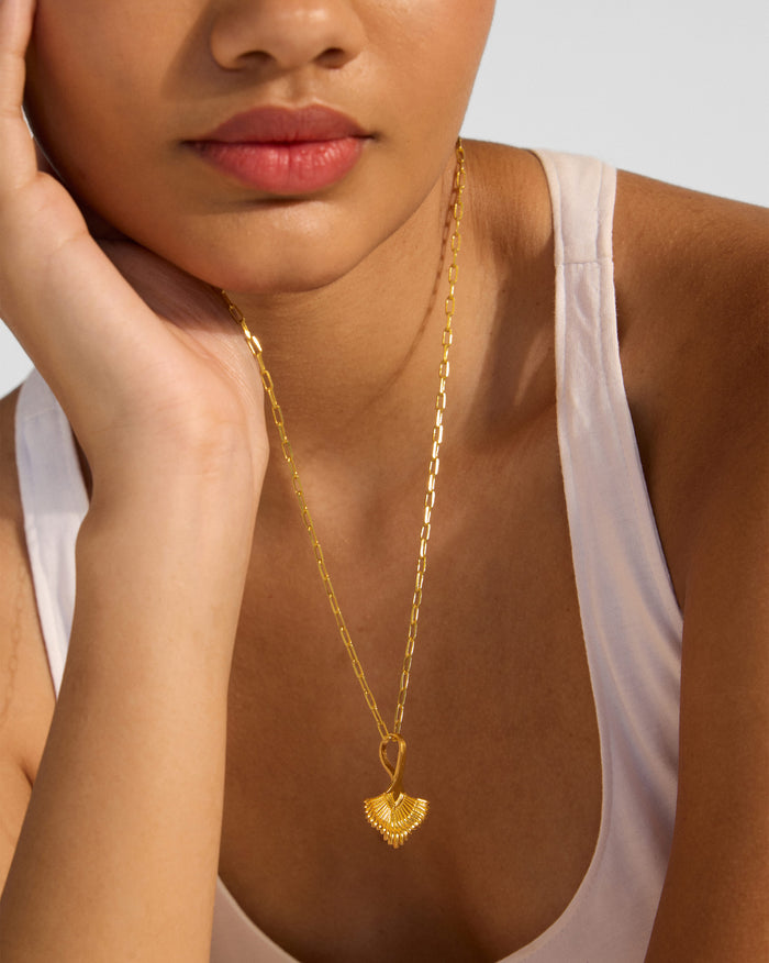 Close-up of a gold palm necklace pendant with ribbed texture on a person.