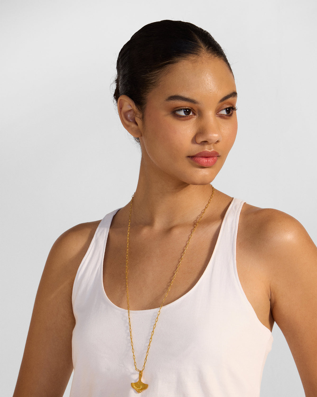Person wearing a gold palm necklace with a leaf pendant.