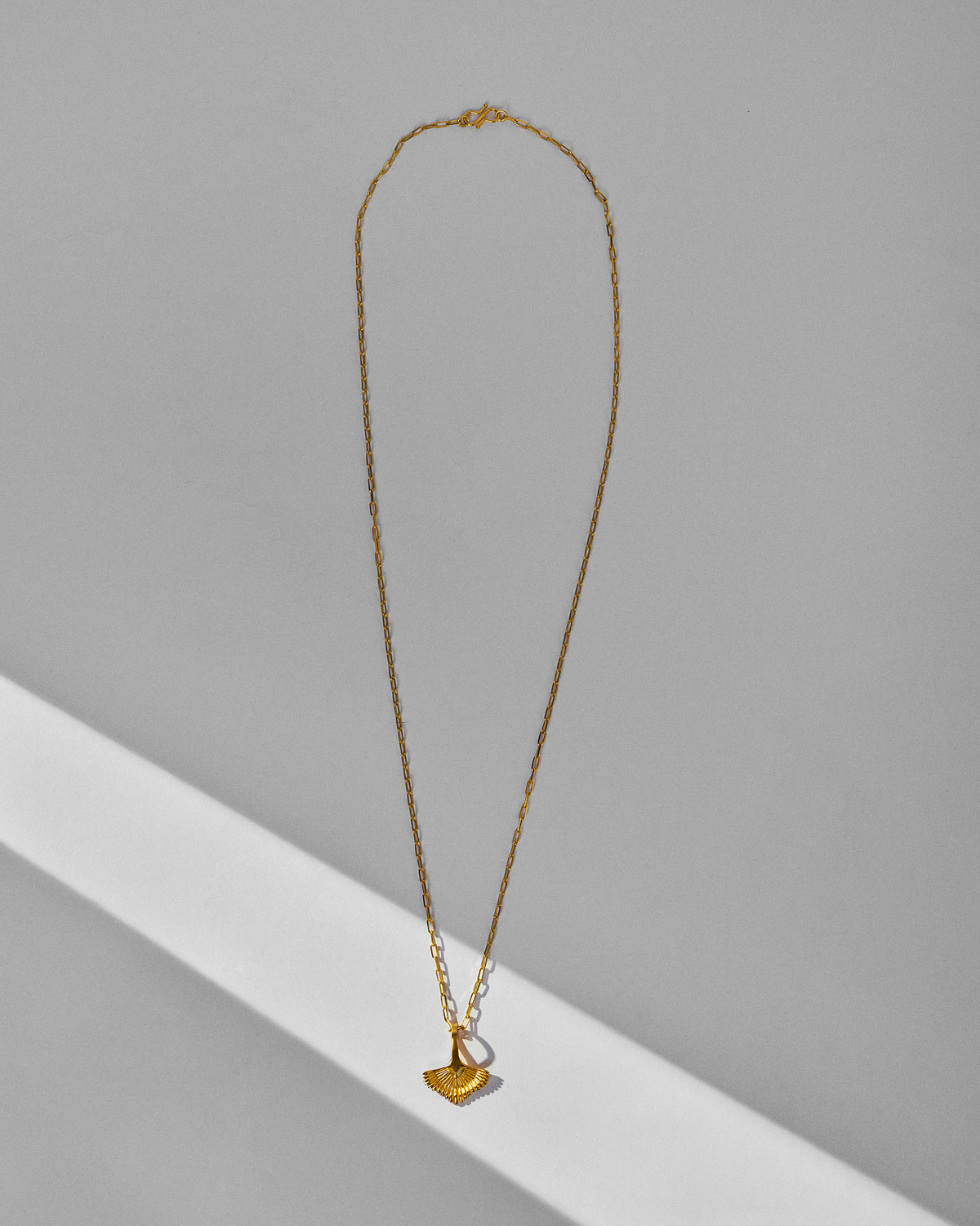 Gold palm necklace hanging against a light wall.