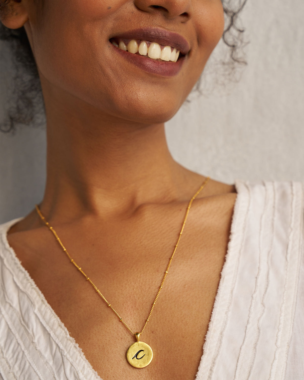 Gold Alphabet C charm with a black lowercase c worn on a chain.