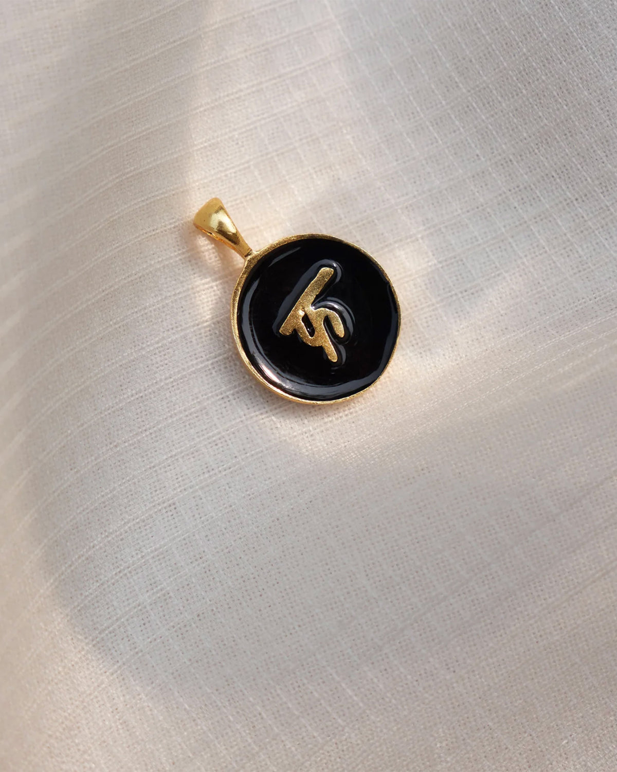 Close-up of a black enamel alphabet charm with a raised gold letter.