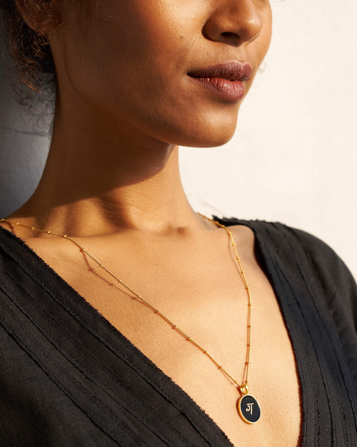 Alphabet G charm in black and gold worn on a fine gold chain.
