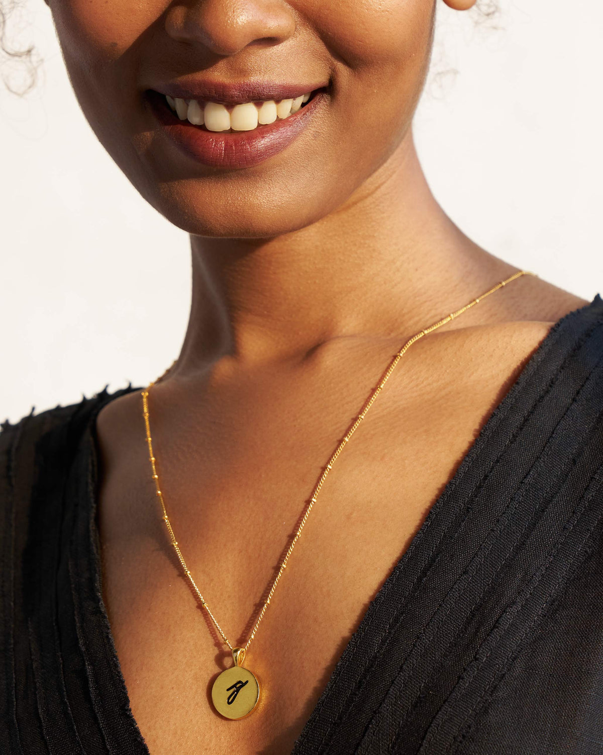Person wearing a gold alphabet charm on a fine chain.