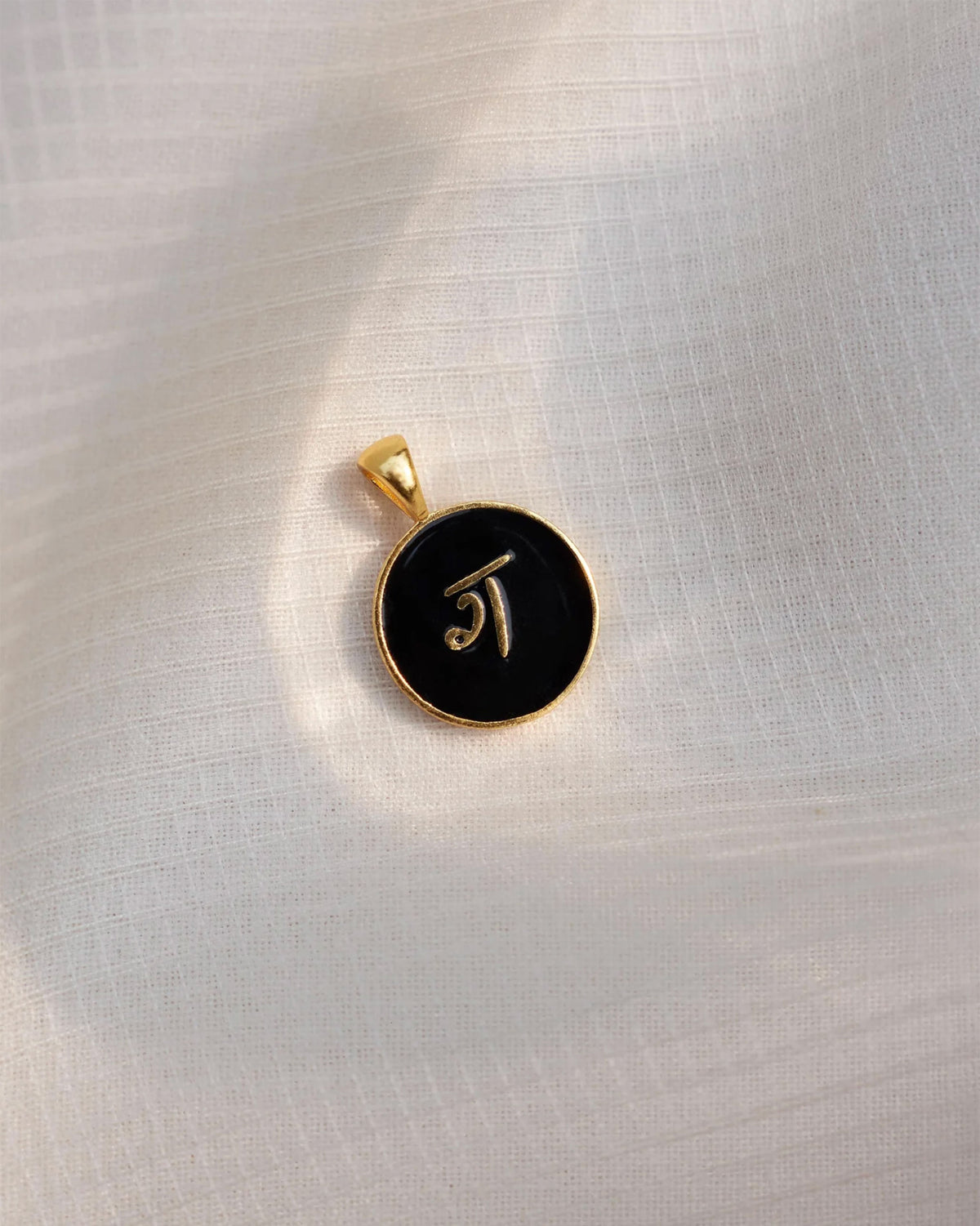 Close-up of a black and gold Alphabet G charm showing ग.
