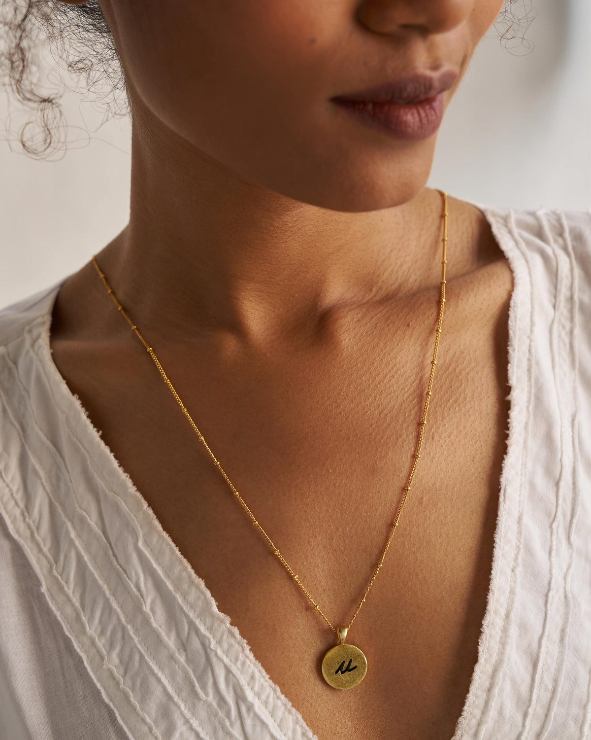 Gold Alphabet U charm with a black script letter u when worn.