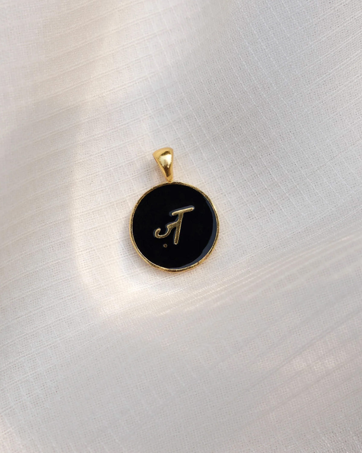 Close-up of a black and gold Alphabet Z charm showing a Devanagari letter.