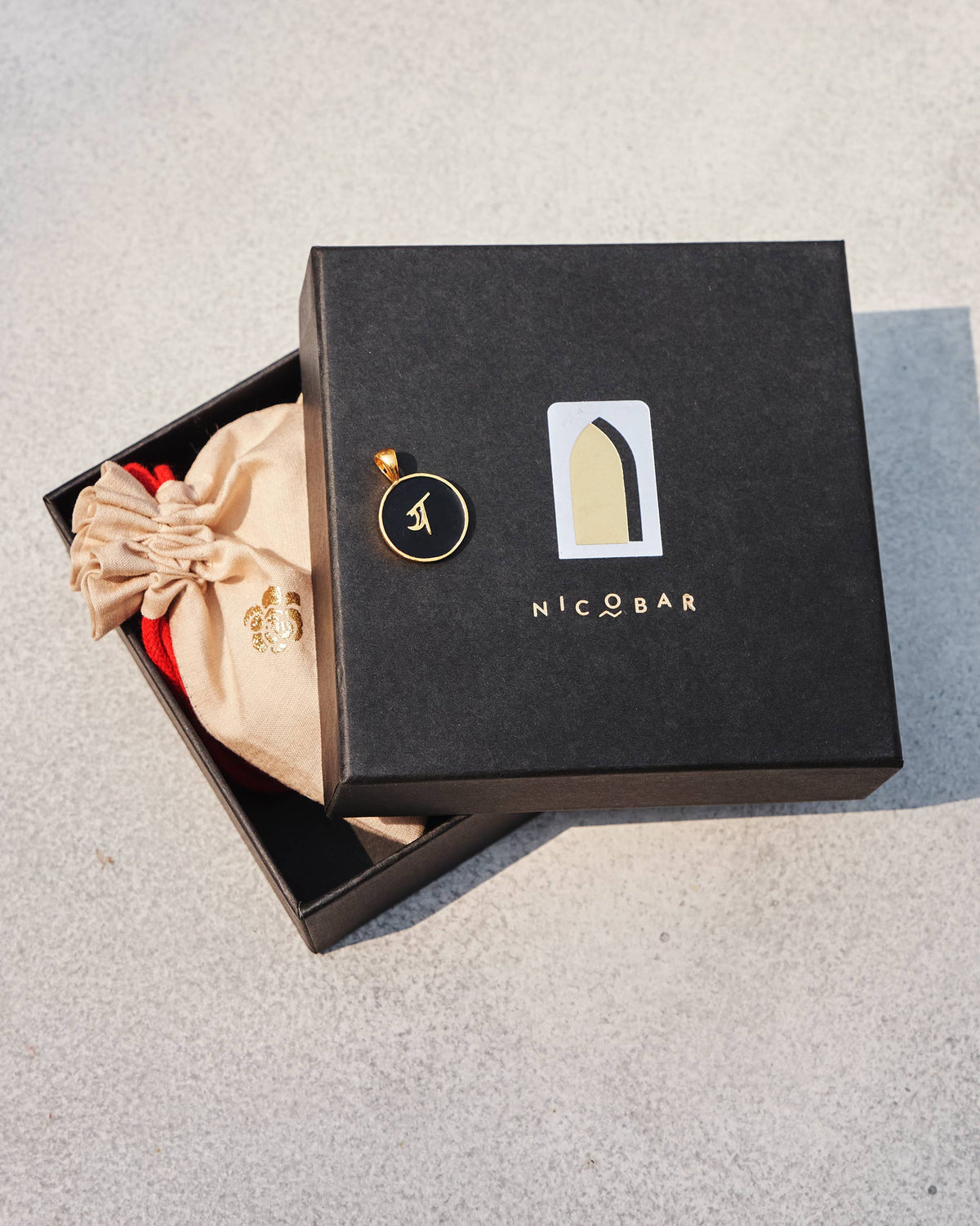 Black and gold Alphabet Y charm with य on a Nicobar gift box.