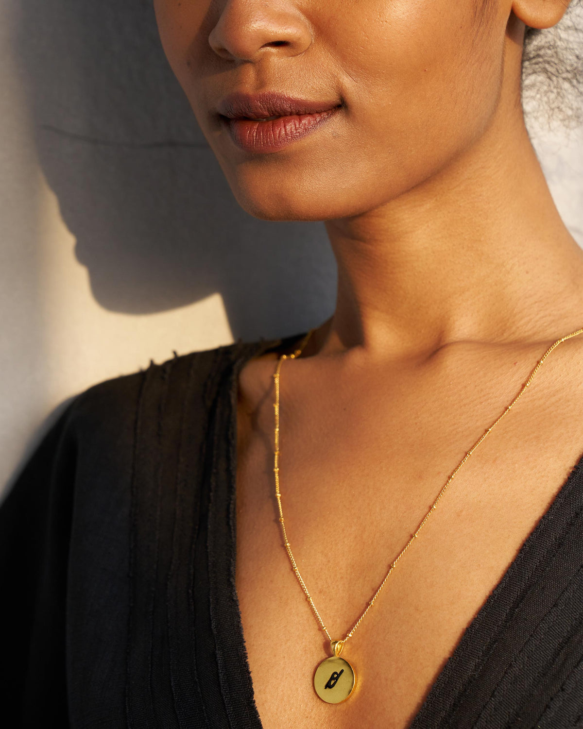 Gold Alphabet O charm with a black script letter o when worn.