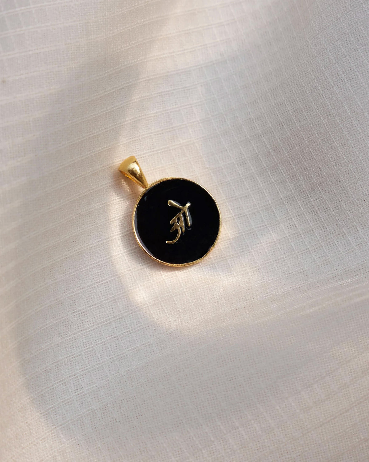 Close-up of a black and gold Alphabet O charm showing a Devanagari letter.