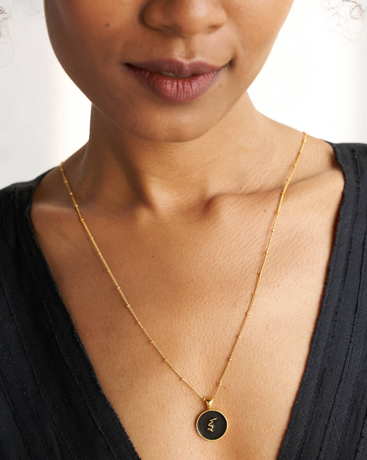 Black and gold Alphabet I charm with इ worn on a satellite chain.